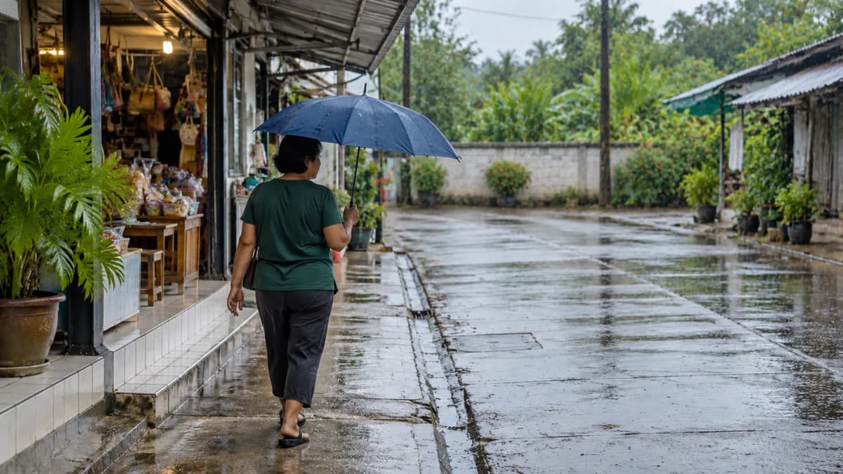 A woman walks with an umbrella beside small shops on a wet Thai lane.