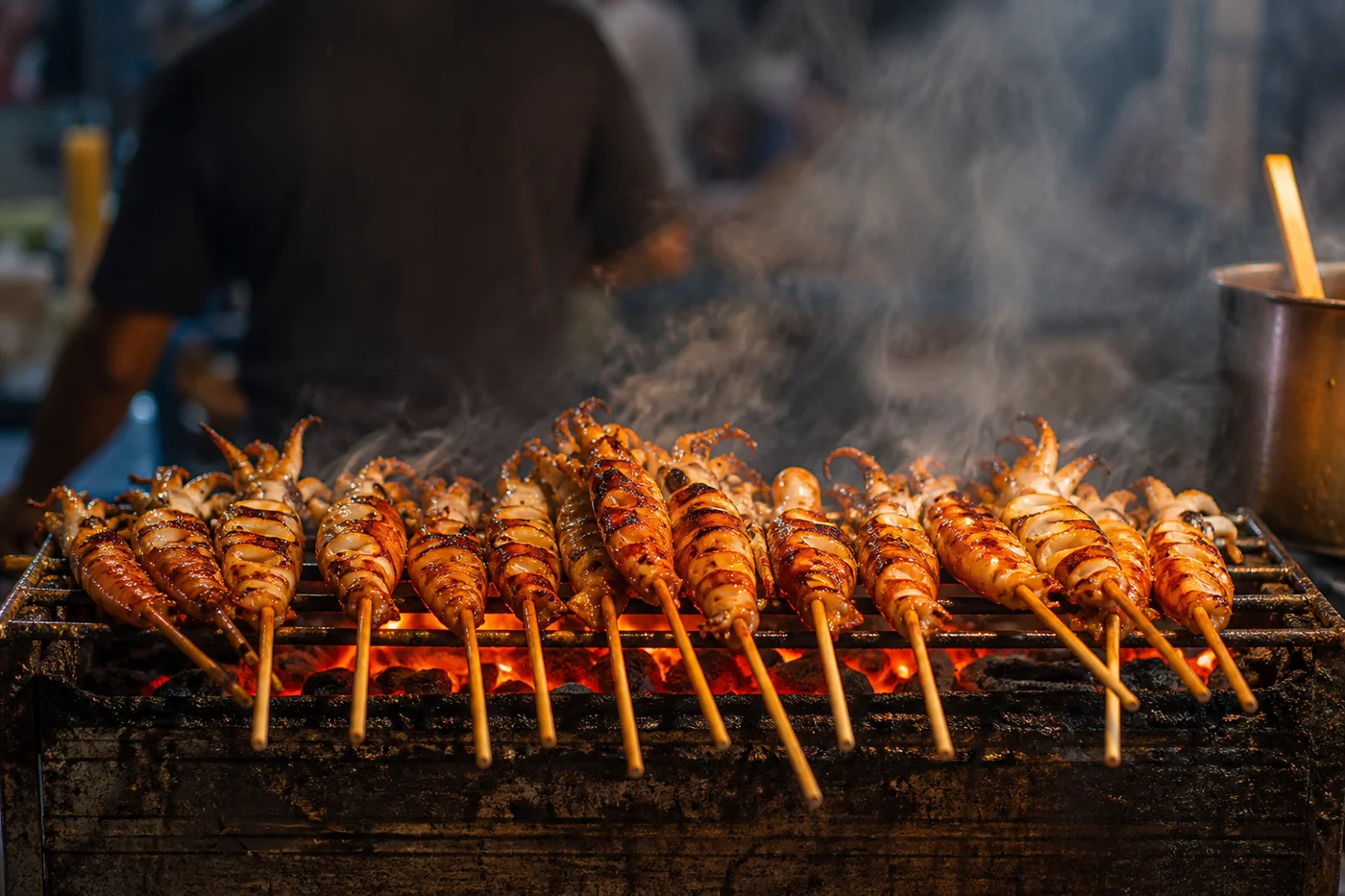 Grilled seafood skewers on charcoal grill with smoke rising at Hua Hin night market